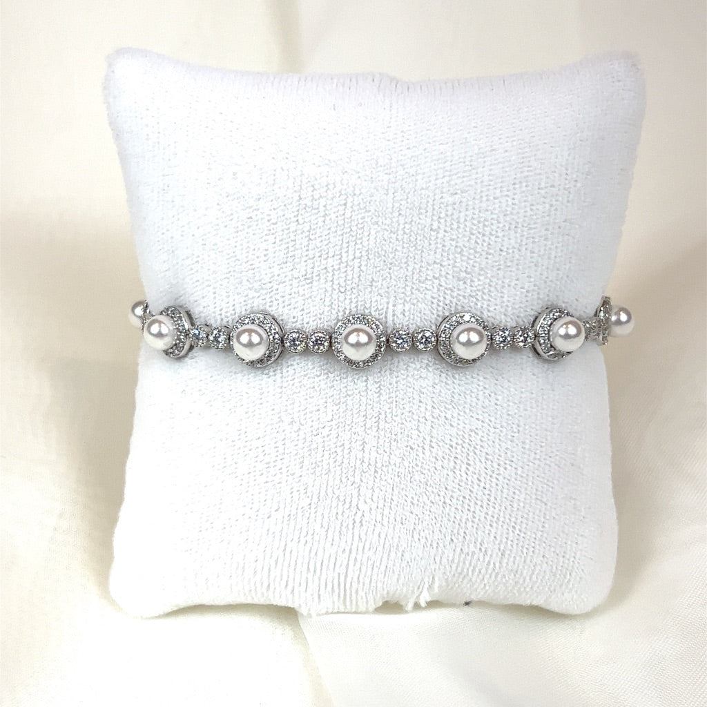The Luxurious Bridal Bracelet (style no. HGB1986) sits elegantly on a white cushion, echoing a Swarovski bridal tiara with spherical pearls and cubic zirconia in intricate settings for a lavish appearance.