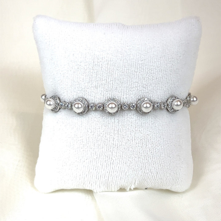 The Luxurious Bridal Bracelet (style no. HGB1986) sits elegantly on a white cushion, echoing a Swarovski bridal tiara with spherical pearls and cubic zirconia in intricate settings for a lavish appearance.