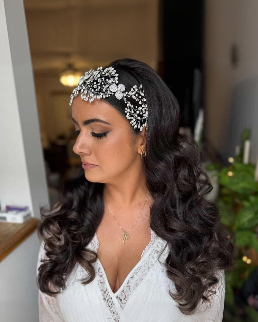 Bride in profile, eyes closed, wearing Swarovski crystal face-framing headpiece with floral vine design over dark waves