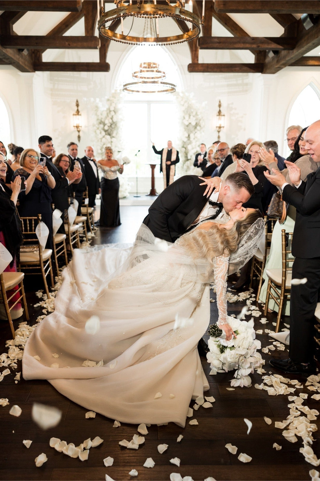 Bride and groom's dramatic first kiss dip showcasing custom royal cathedral veil with crystal and beading embroidery flowing across chapel aisle