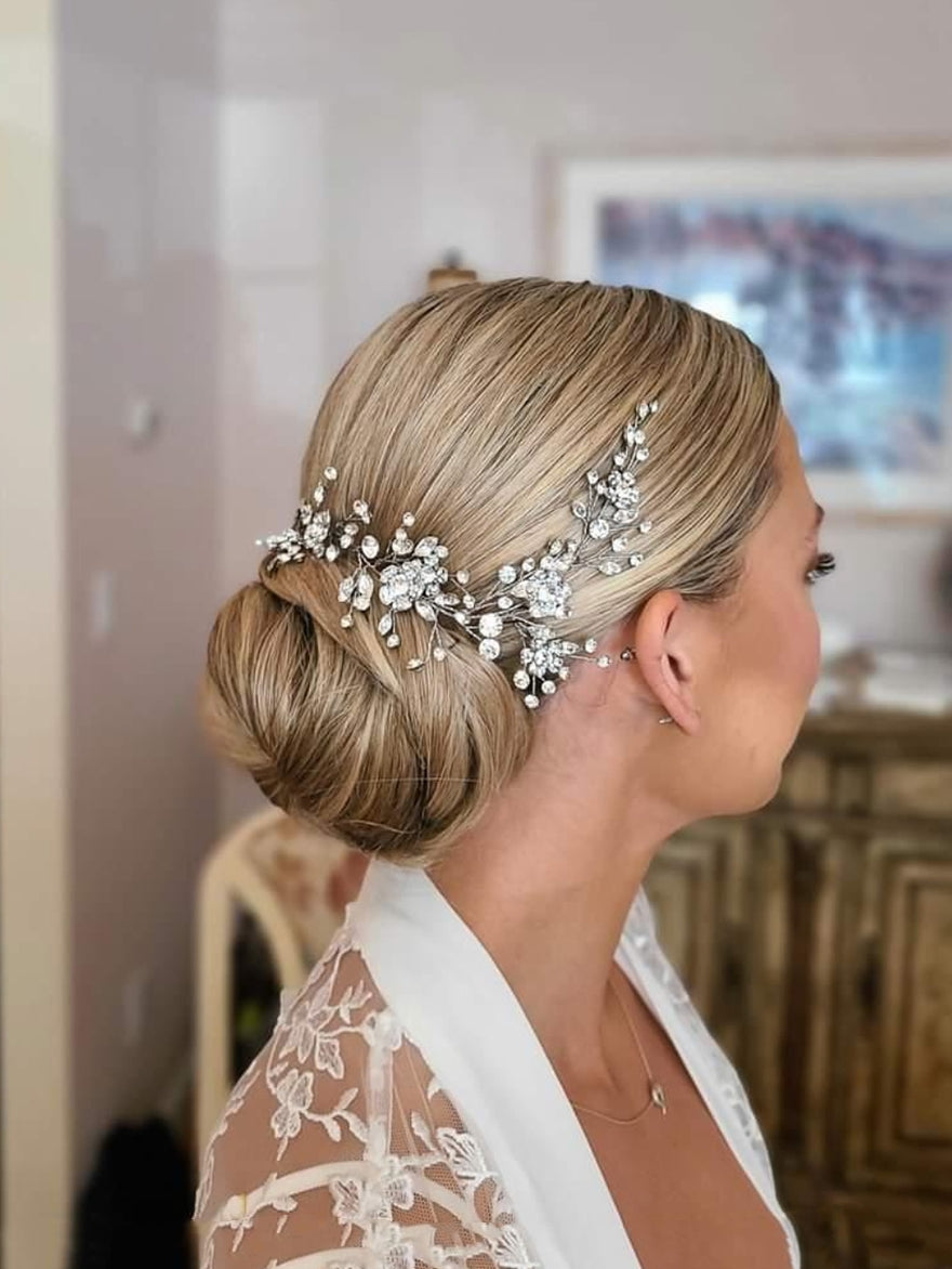 a lovely bride looks off to one side. Her blonde hair is in a low bridal bun adorned with a crystal bridal hair vine