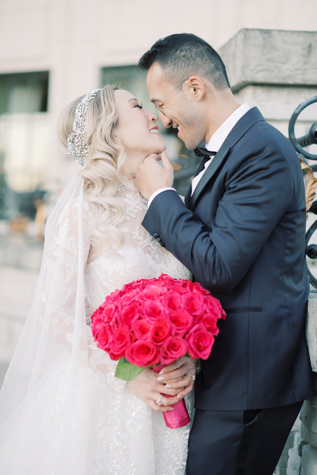 A beautiful bride and her handsome groom smile at each other. The bride holds a magenta bouquet. 
