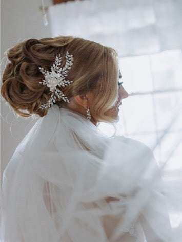 A bride with her hair up in a romantic updo adorned with a custom bridal comb of porcelain flowers, pearls,and crystals with matching dangling earrings