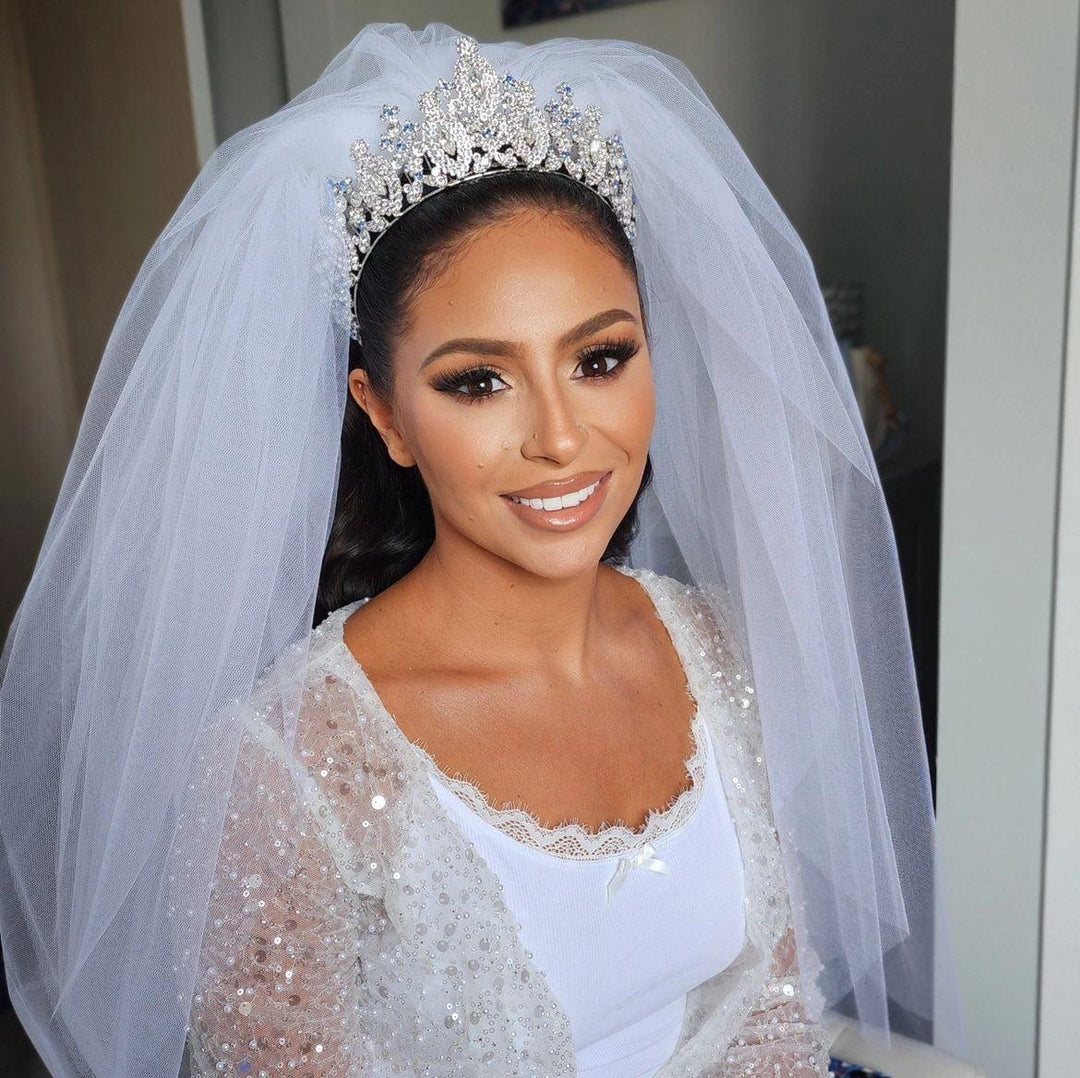 A beautiful bride smiling and wearing her custom wedding tiara with blue stones and a full, fluffy bridal veil