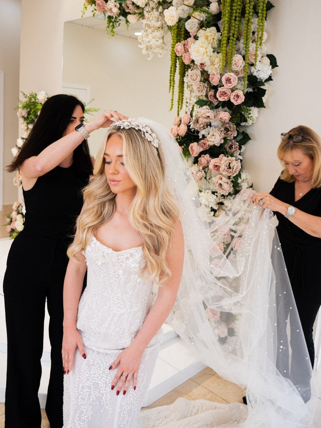 Bridal Styles Boutique stylist placing a crystal floral headpiece on a bride wearing a strapless beaded gown and pearl-dotted veil