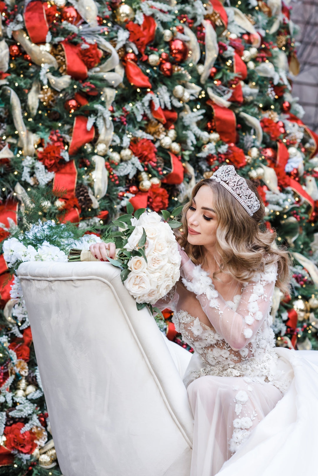 Bride wearing a dazzling crystal wedding crown and romantic floral appliqué wedding gown holding white rose bouquet in front of Christmas tree
