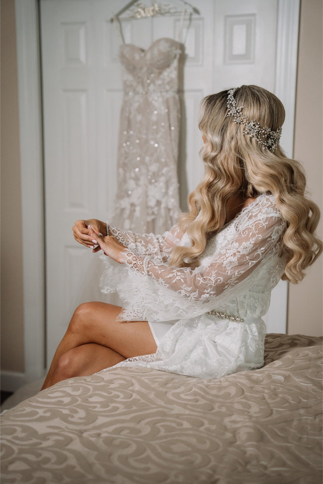Bride Lauren getting ready in lace robe with her custom freshwater pearl and crystal halo headpiece styled in soft blonde waves, wedding dress visible in background