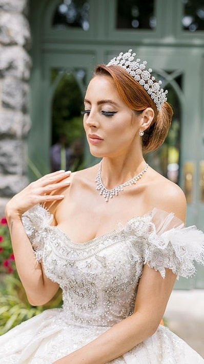 Bride wearing elegant pearl and crystal tiara with romantic off-shoulder lace gown, showcasing 2026 wedding headpiece trends