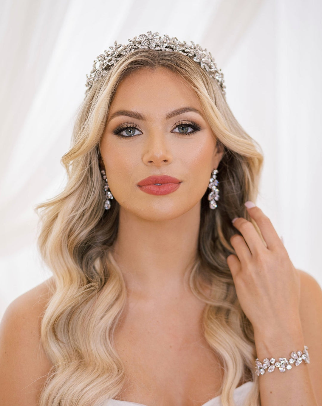 Blond bride with wavy hair wearing a crystal headpiece, long floral earrings and matching floral bracelet