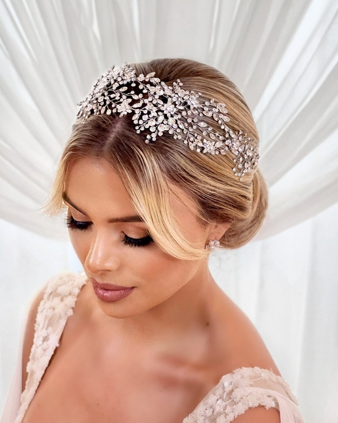 Blond bride wearing a crystal-encrusted hair vine headpiece that looks like a flower garland  with a low bun 