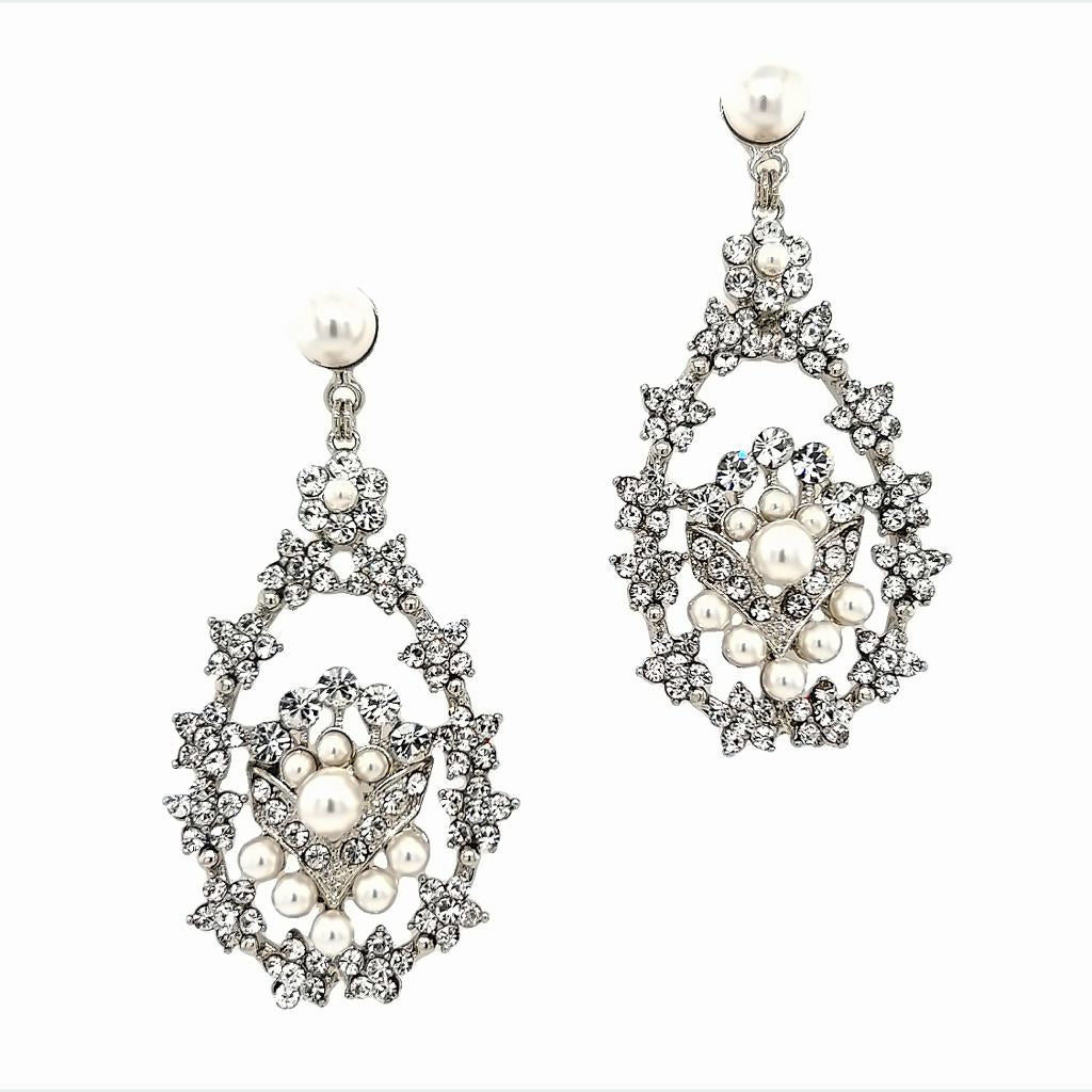 Close-up of Swarovski crystal chandelier earrings with pearl accents, featuring an ornate open teardrop design and floral-inspired details in silver-tone metal.
