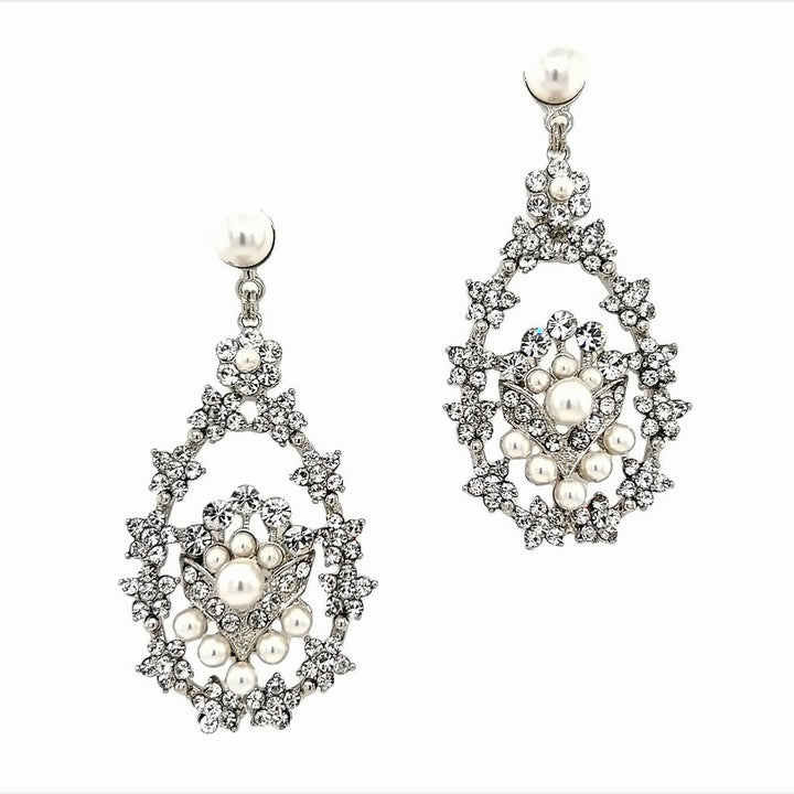Close-up of Swarovski crystal chandelier earrings with pearl accents, featuring an ornate open teardrop design and floral-inspired details in silver-tone metal.