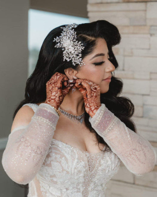 Beautiful dark hair bride putting on an earing wearing a Swarovski crystal headpiece with sprays and flowers by Bridal Styles Boutique