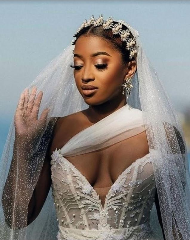 Beautiful black bride wearing a pearl and crystal bridal headband headpiece and matching bridal earrings touching her veil.