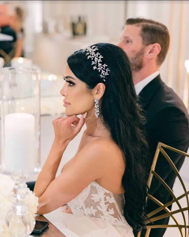 Dark hair bride looking in the distance next to her husband. She is wearing a crystal headband headpiece and vine earrings by Bridal Styles Boutique