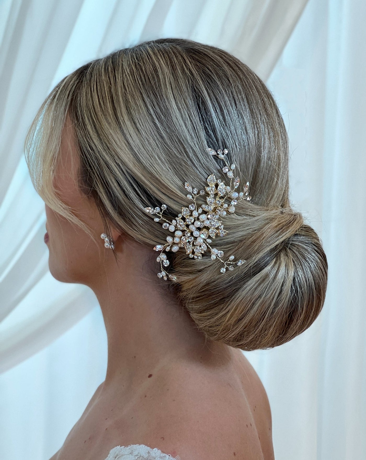 female model wearing gold bridal hair comb with small encrusted leaves and curved sprigs of crystal and pearl above an updo