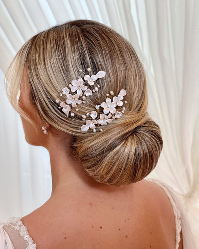 female model wearing two small bridal hair combs with porcelain flowers and small sprigs of crystal and pearl above an updo