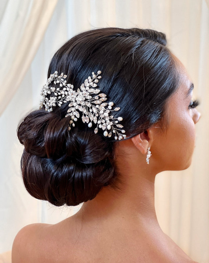 A woman with a smooth, elegant updo is adorned with the Stunning Swarovski Crystal Bridal Hair Vine (style no. 242594). She also wears delicate drop earrings, all set against a softly blurred background.