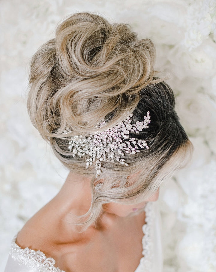 A woman with an elegant updo hairstyle features the shimmering Swirling Pearl and Crystal Bridal Hair Comb, style no. 242580. The soft white background enhances her white attire.