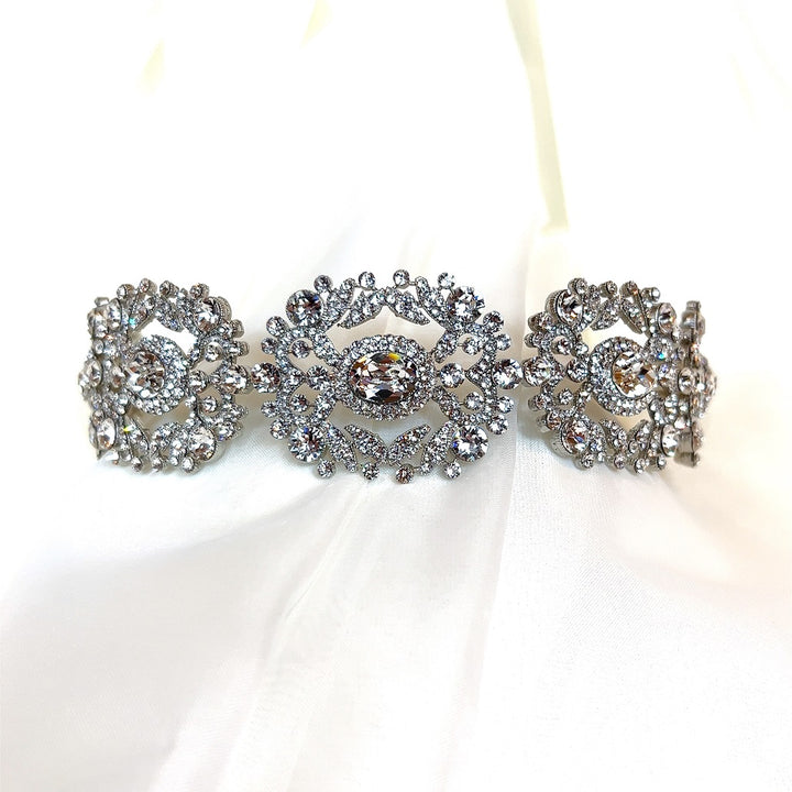 The Ornate Crystal Bridal Headband (Style no. 242737) features intricate silver floral designs and sparkling crystal accents, exuding elegance on a white fabric background, perfect for bridal wear.