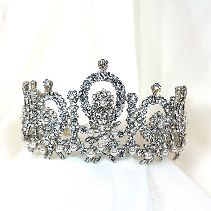 The Regal Wedding Crown, style no. 80015, is a stunning bridal crown featuring an intricate design of  pearls, and Swarovski crystals on a soft white base. Its ornate patterns offer an elegant and regal touch for a bridal look.