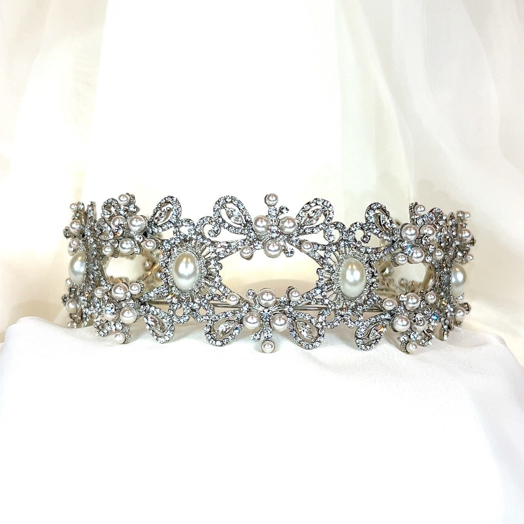 A Vintage Inspired Pearl and Swarovski Crystal Headband (style no. 80055), featuring ornate floral designs with pearls and crystals, is displayed against a soft white fabric background.
