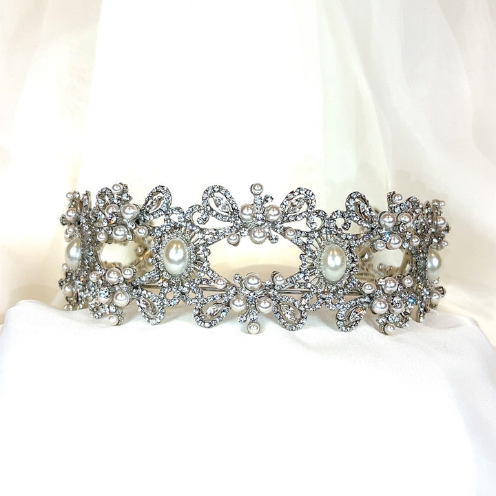 A Vintage Inspired Pearl and Swarovski Crystal Headband (style no. 80055), featuring ornate floral designs with pearls and crystals, is displayed against a soft white fabric background.