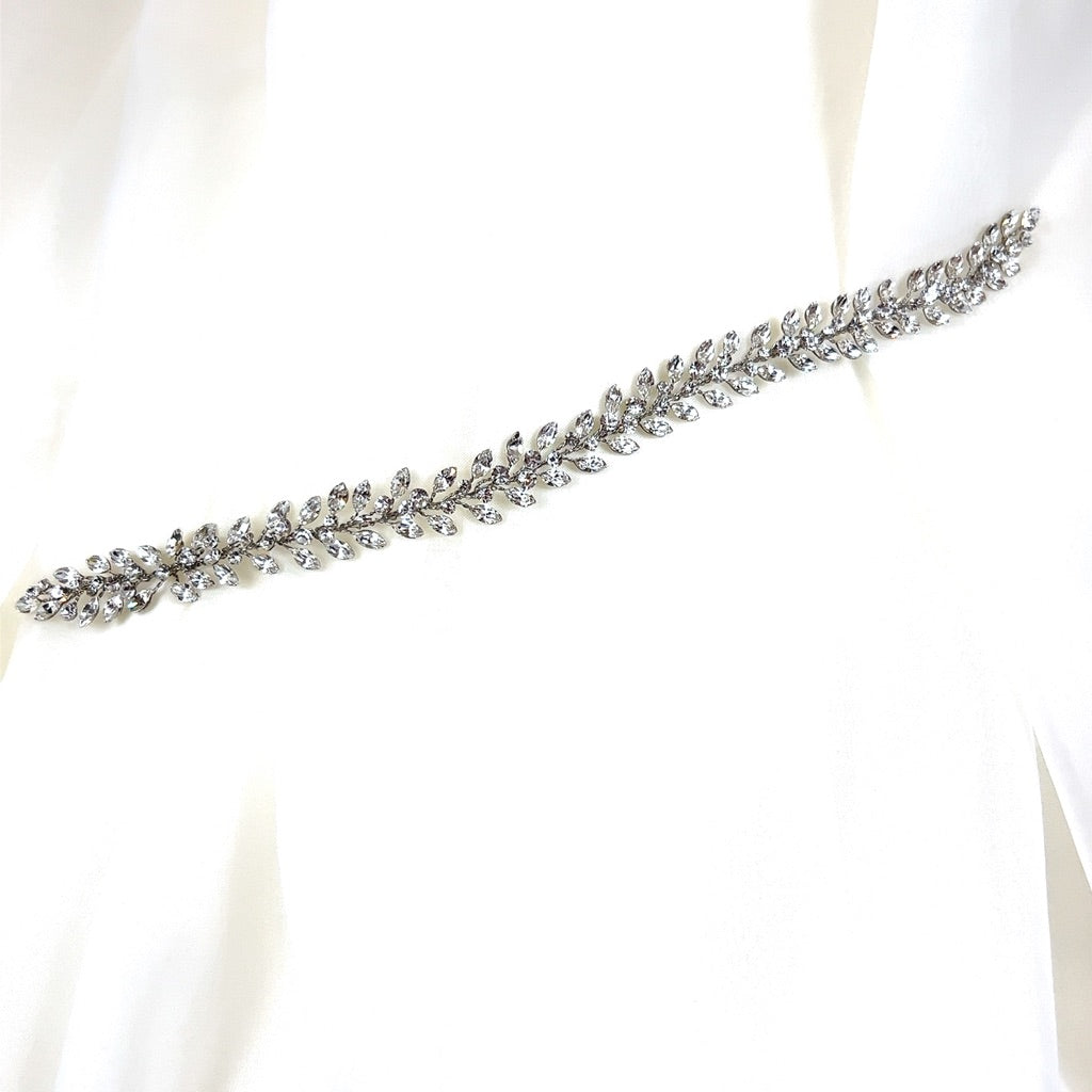 Laid over smooth, white fabric, the Traditional Crystal Vine style no. 242710 belt features a delicate silver-toned design with leaf motifs and sparkling Swarovski crystals.