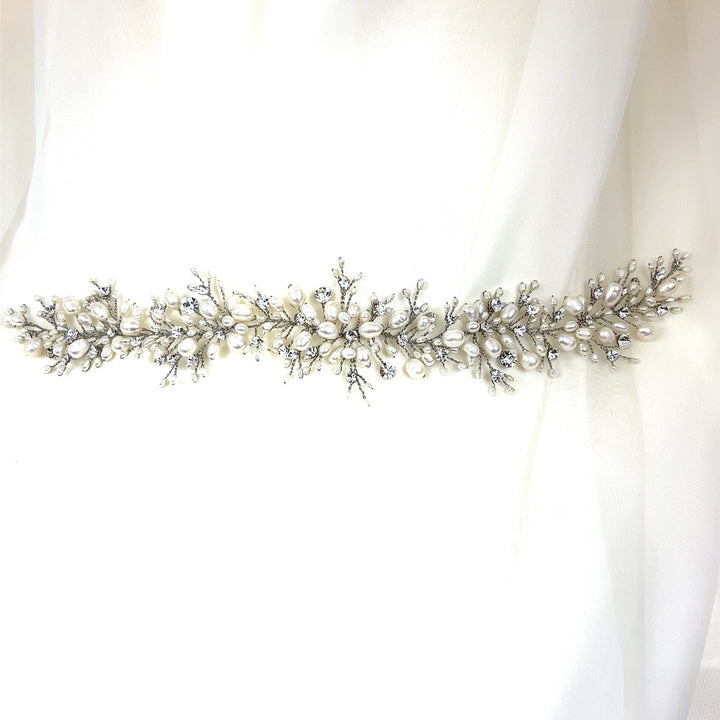 The Cluster Pearl and Crystal Bridal Vine (style no. 242704) features intricate branches with clusters of pearls and sparkling Swarovski crystals on a white fabric background, offering an elegant, delicate look similar to a Swarovski bridal tiara.