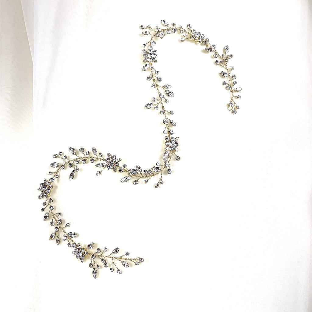 The Dainty Crystal and Flower Hair Vine, style no. 39718871, is a delicate and ornate Swarovski crystal wedding hairpiece adorned with small sparkling crystals, arranged in a serpentine design on a plain white background.