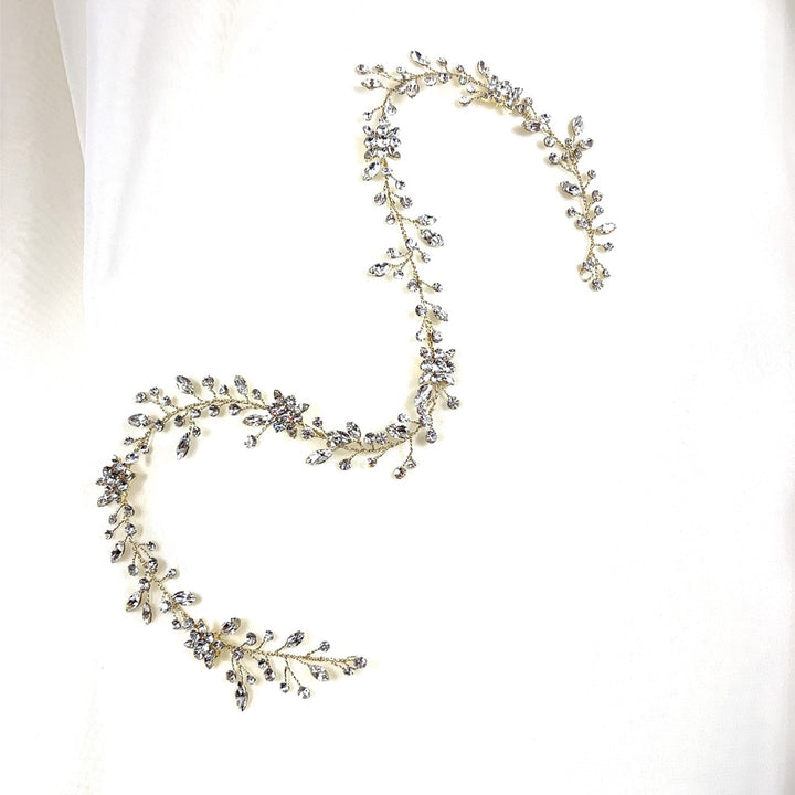 The Dainty Crystal and Flower Hair Vine, style no. 39718871, is a delicate and ornate Swarovski crystal wedding hairpiece adorned with small sparkling crystals, arranged in a serpentine design on a plain white background.