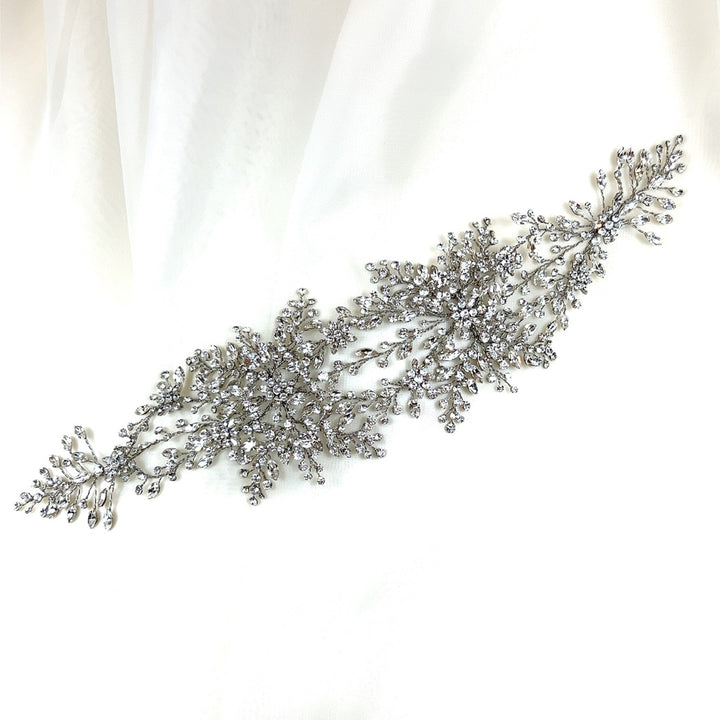The Shimmering Bridal Vine style no. 242480 is a sparkling silver bridal hair accessory with Swarovski crystal and bead detailing in floral and vine patterns, elegantly displayed on a white fabric background.