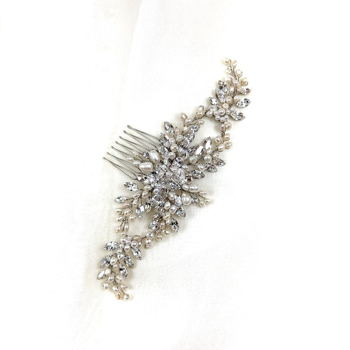 The Flowing Cluster Hair Comb (style no. 242514) showcases intricate floral and leaf designs, adorned with pearls and genuine crystals, elegantly laid on soft white fabric.