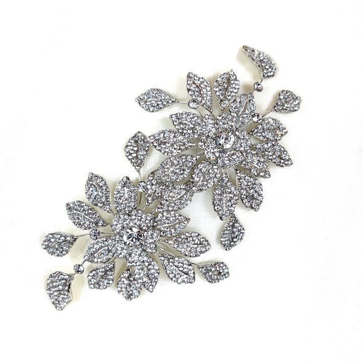 The Dazzling Double Blossom Bridal Hair Comb, style no. 80065, features two ornate and sparkling brooches with large flower designs made of intricately arranged Swarovski crystals. 