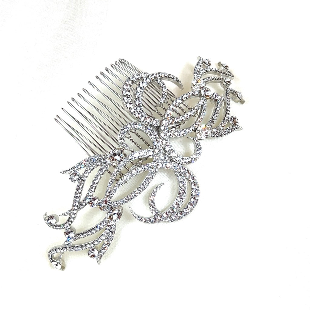 The Elegant Crystal Swirl Comb (style no. 242634) showcases luxurious silver swirls of Swarovski crystals, offering a luxurious floral and leaf design. It's displayed against a plain white background.