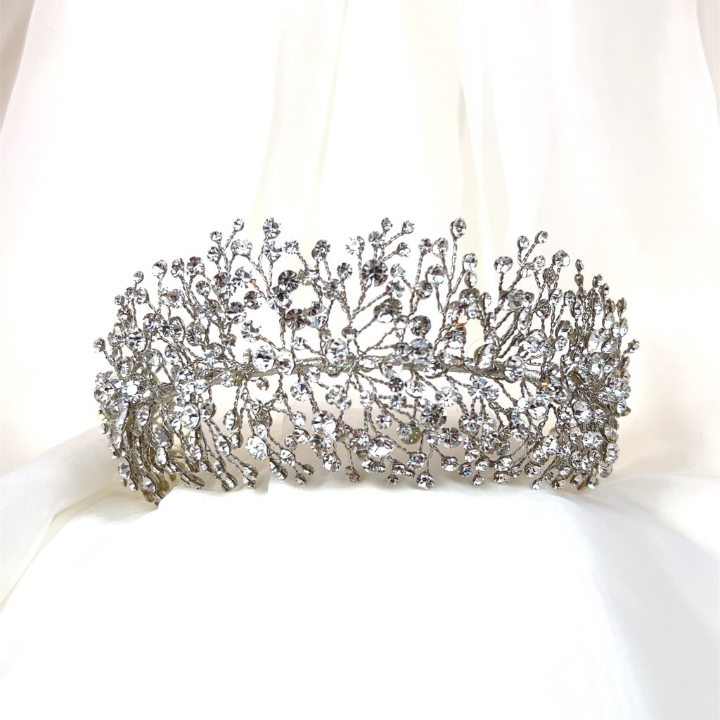 The Bursting Swarovski Crystal Headband (style no. 3910361) is an ornate and bold Swarovski crystal headband designed in a delicate pattern resembling branches. It is beautifully displayed against a soft white fabric background.