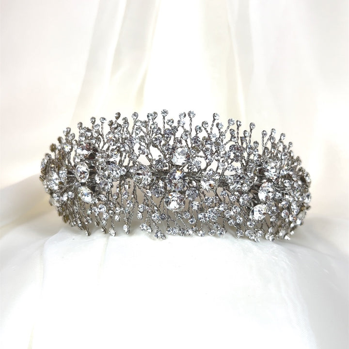 The Bold and Beautiful Swarovski Crystal Headband (style no. 391022) features a design with intricate, branch-like patterns against a delicate white fabric, embellished with numerous glittering gemstones.