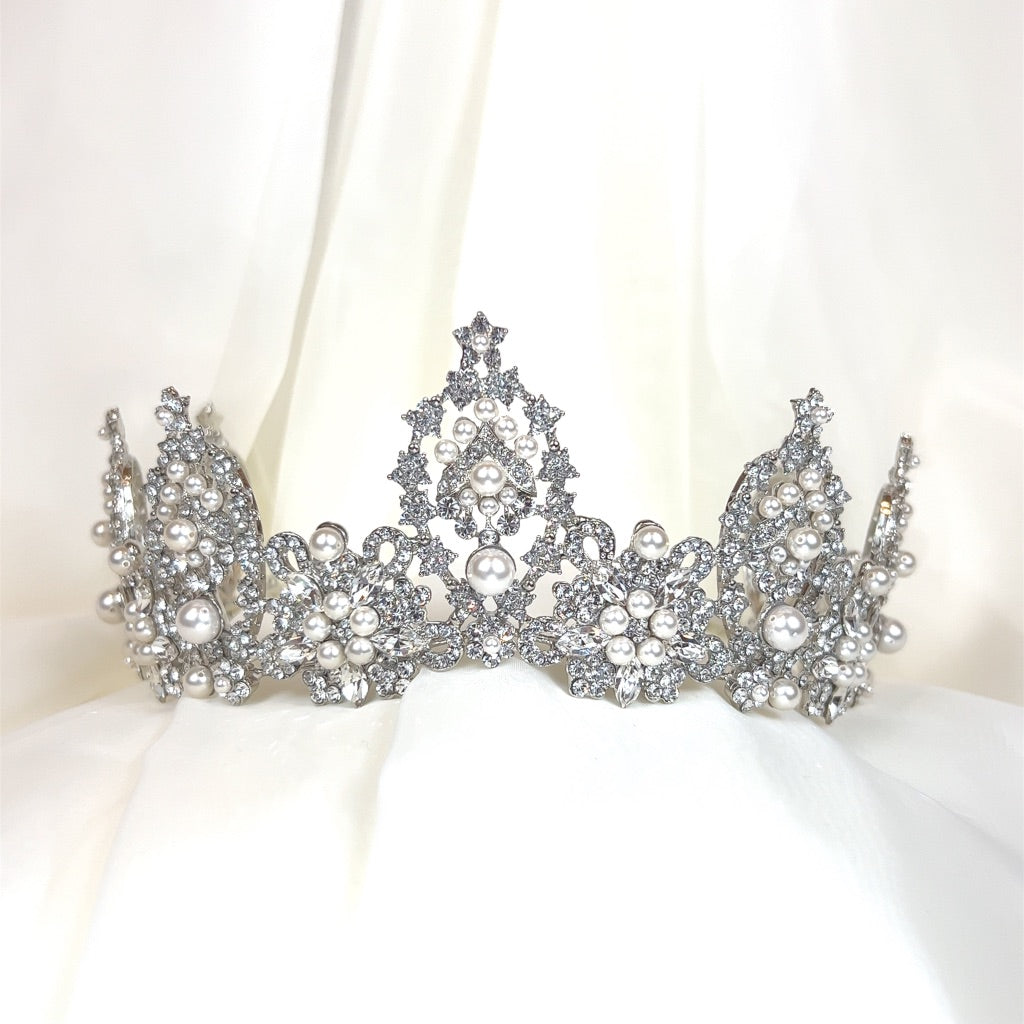 The Regal Bridal Crown style no. 80038 is a Swarovski crystal wedding crown featuring intricate lace-like patterns, pearl accents, and sparkling gems.
