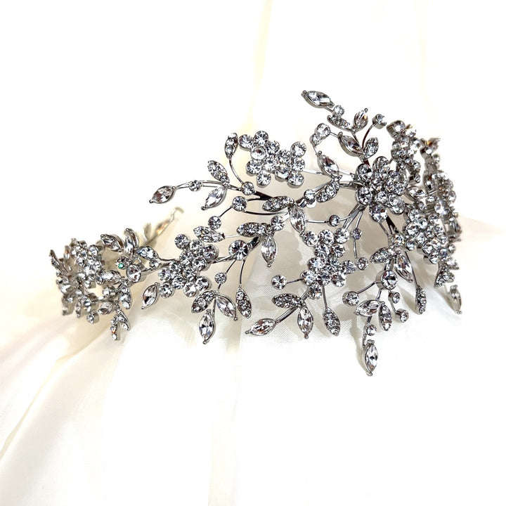 The Asymmetrical Swarovski Crystal Flower Bridal Headband (style no. 242729) dazzles with its intricate floral and leaf designs, exuding elegance and luxury. Displayed against a white background.