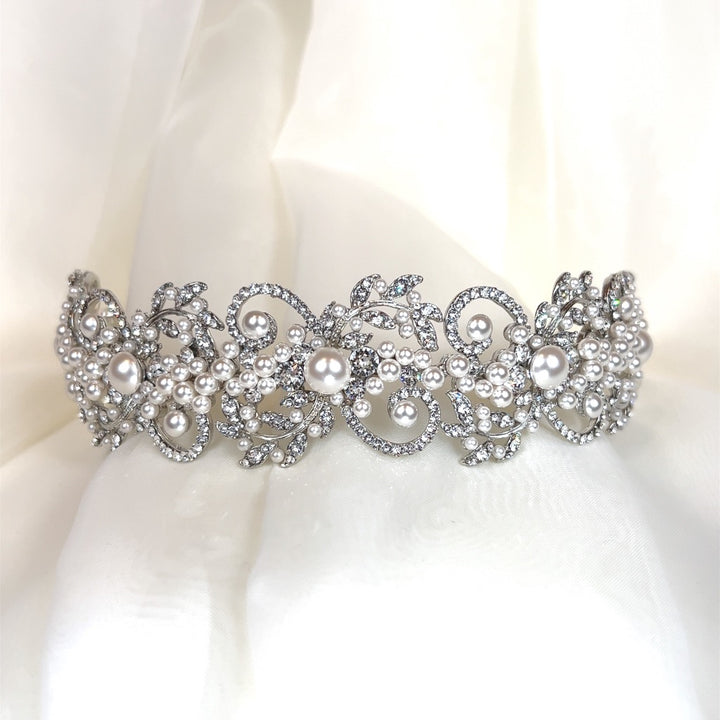 A Swirling Pearl and Swarovski Crystal Headband (style no. 242706), intricately decorated with pearls and sparkling crystals, is elegantly displayed on a soft white fabric background.