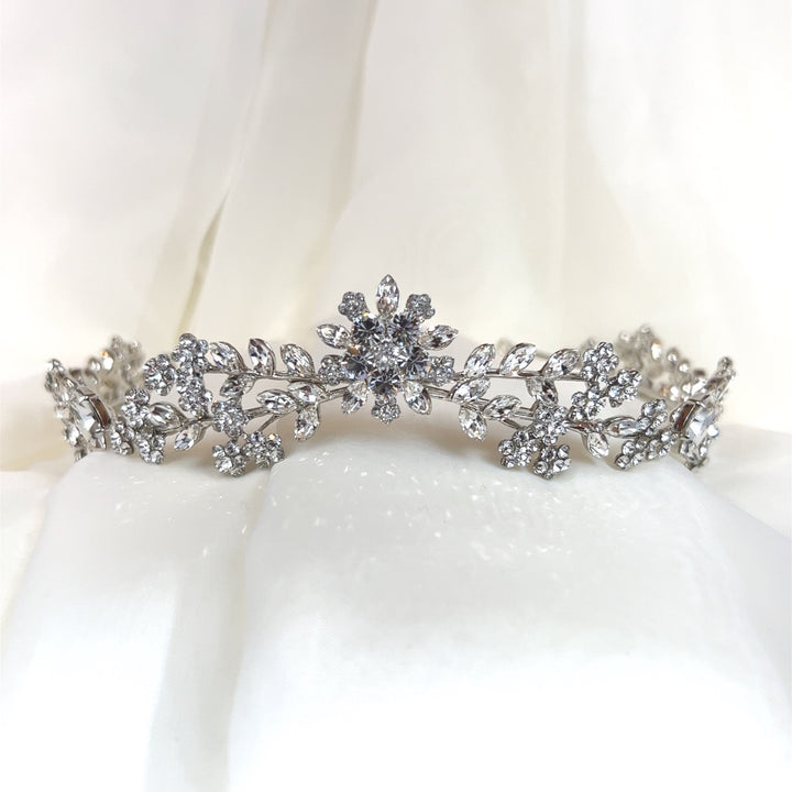 A delicate Swarovski Crystal Floral Tiara (style no. 80008, featuring sparkling floral and leaf patterns set against a soft, white fabric background.