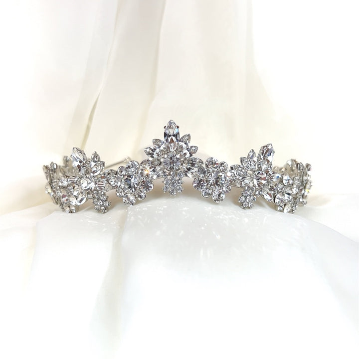 The Floral Crystal Bridal Tiara style no. 80057, a Swarovski bridal piece with intricate floral designs against a soft white fabric background, exudes elegance and sophistication.