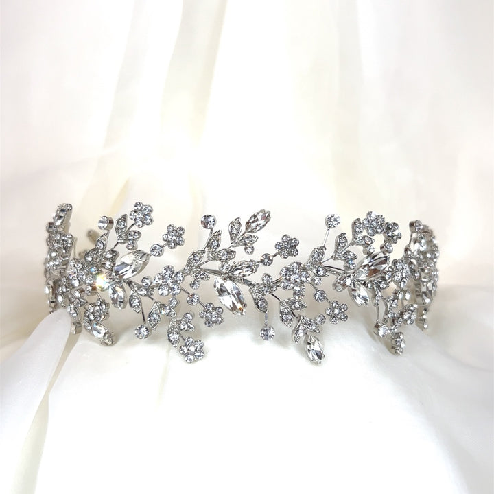 The Dainty Crystal Bridal Headband (style no. 242684), featuring intricate silver floral and Swarovski crystal leaf designs, is elegantly showcased against a soft white fabric backdrop.