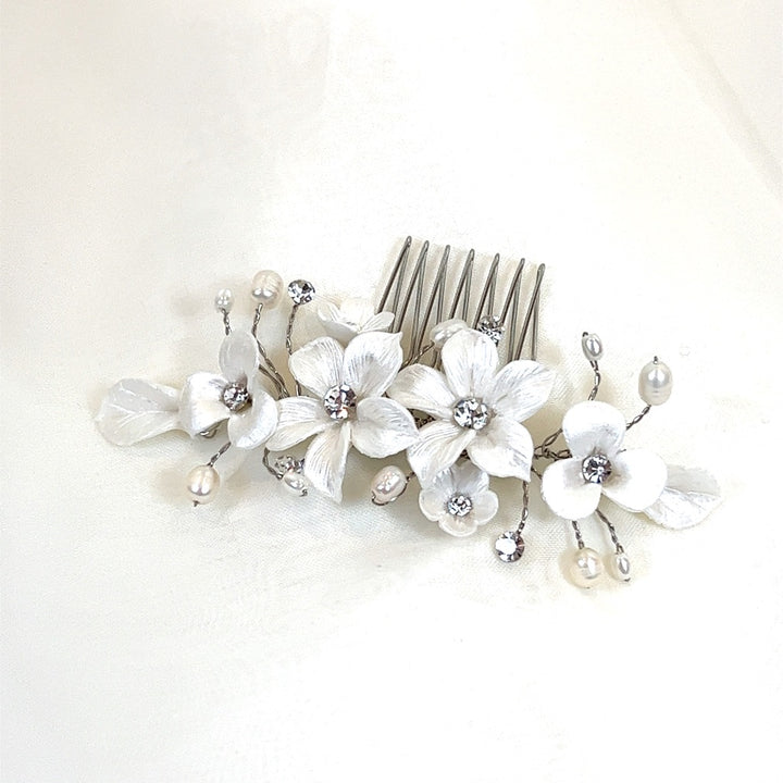 The Romantic Porcelain Flower Hair Comb (style no. 242724) is a delicate Swarovski crystal headpiece featuring dainty ceramic flowers, pearl accents, and crystals. Its elegant design with three prominent flowers and sprigs.