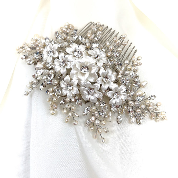 Close-up of a Swarovski crystal wedding  comb adorned with white porcelain flowers, sparkling crystals, and freshwater pearls on a soft ivory fabric background