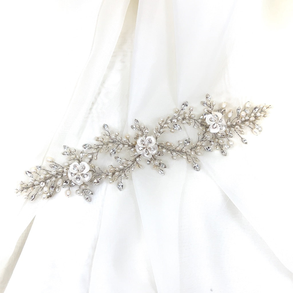 A intricate and delicate Swarovski bridal hair vine featuring floral and leaf designs displayed against a white fabric background.