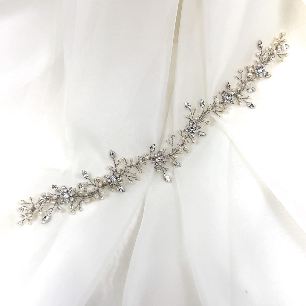 The Sweet Pearl and Crystal Wedding Hair Vine (style no. 242719) is a delicate silver bridal hair comb with intricate floral and leaf designs, adorned with sparkling stones over a sheer white fabric.