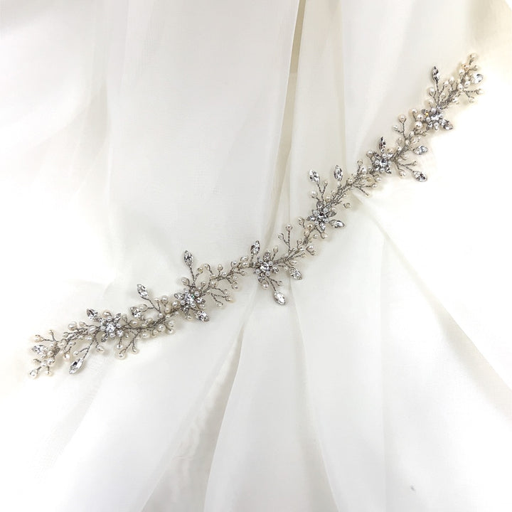 The Sweet Pearl and Crystal Wedding Hair Vine (style no. 242719) is a delicate silver bridal hair comb with intricate floral and leaf designs, adorned with sparkling stones over a sheer white fabric.