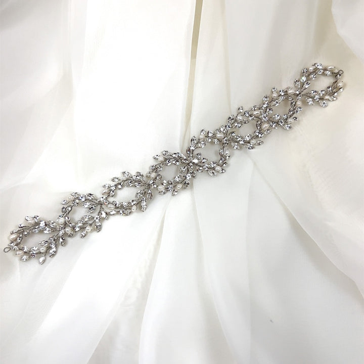 The Classic Pearl and Crystal Looping Vine bridal bracelet, style no. 242644, features intricate leaf and vine designs. It's adorned with small shiny CZ stones and displayed on a soft white fabric background.