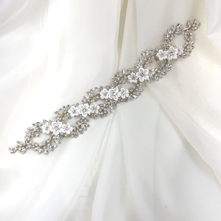 The Elegant Looping Flower Hair Vine style no. 242727, adorned with intricate floral designs and Swarovski crystal embellishments, graces a soft white fabric background.